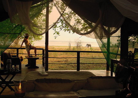 A guest watches from her tent as an elephant strolls along the river bank